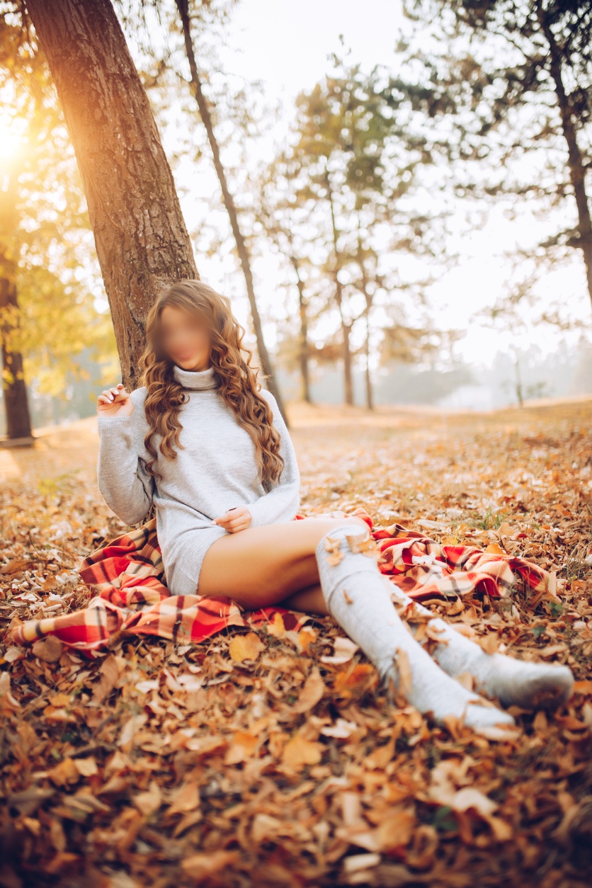 Beautiful woman sits on yellow dry leaves, autumn time. Beautiful sexy bare legs concept epilation, hair removal. Gray long sweater. loose hair. depilation smooth clear skin moisturizing care